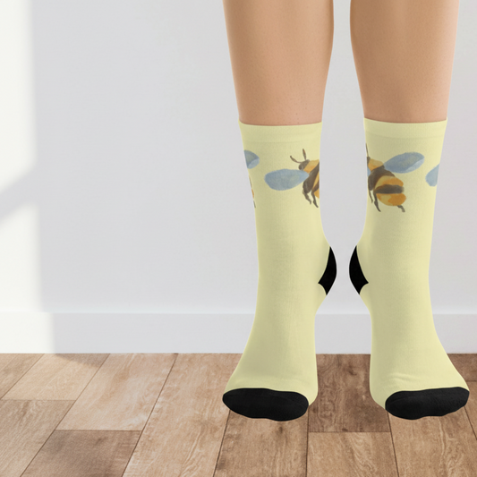 Light yellow socks with bee design worn by a person on a wooden floor.