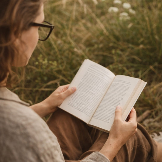 Person reading a book in a natural setting with grass and flowers.