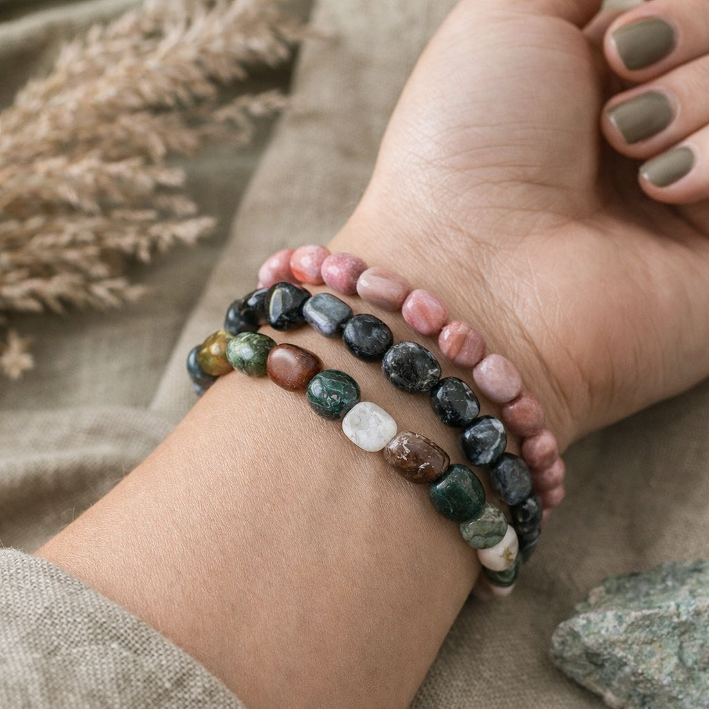 Close-up of a hand wearing multiple  natural stone beaded bracelets on a neutral background
