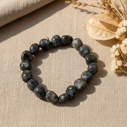 Black stone bead bracelet on a textured beige surface with dried flowers