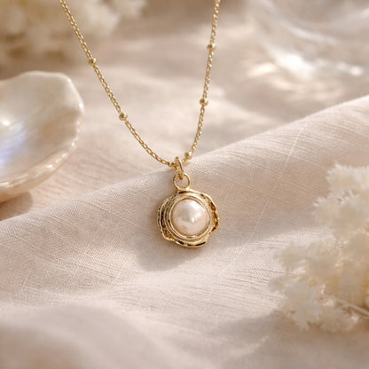 Gold necklace with a pearl pendant on a soft beige fabric background