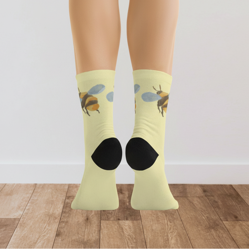 Yellow socks with bee design worn by a person on a wooden floor.