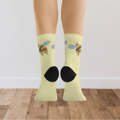 Yellow socks with bee design worn by a person on a wooden floor.