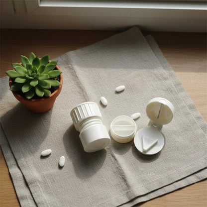 pill cutter and container on a textured surface with scattered pills and a potted plant.