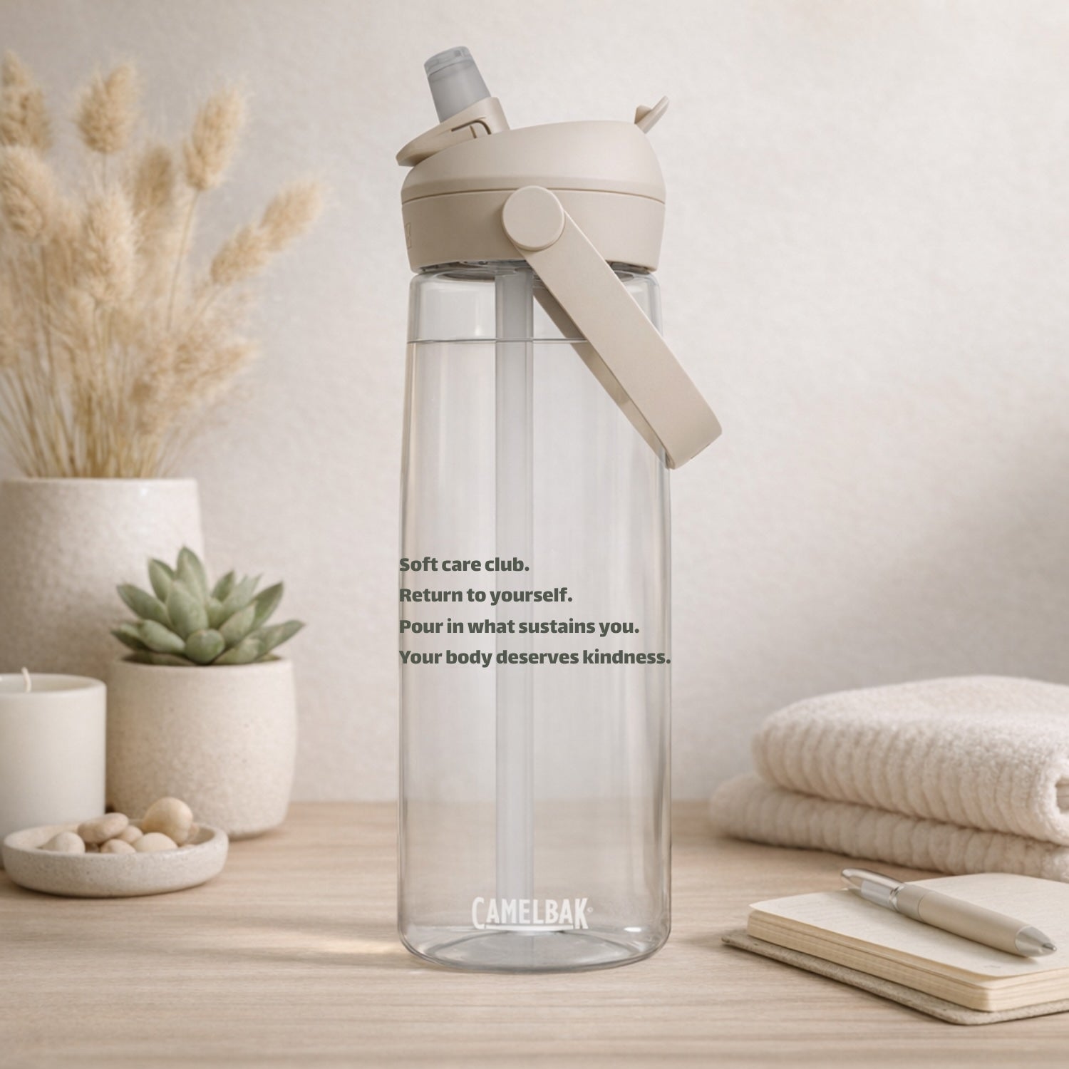 Clear CamelBak water bottle with affirmation phrases and a beige cap on a neutral background